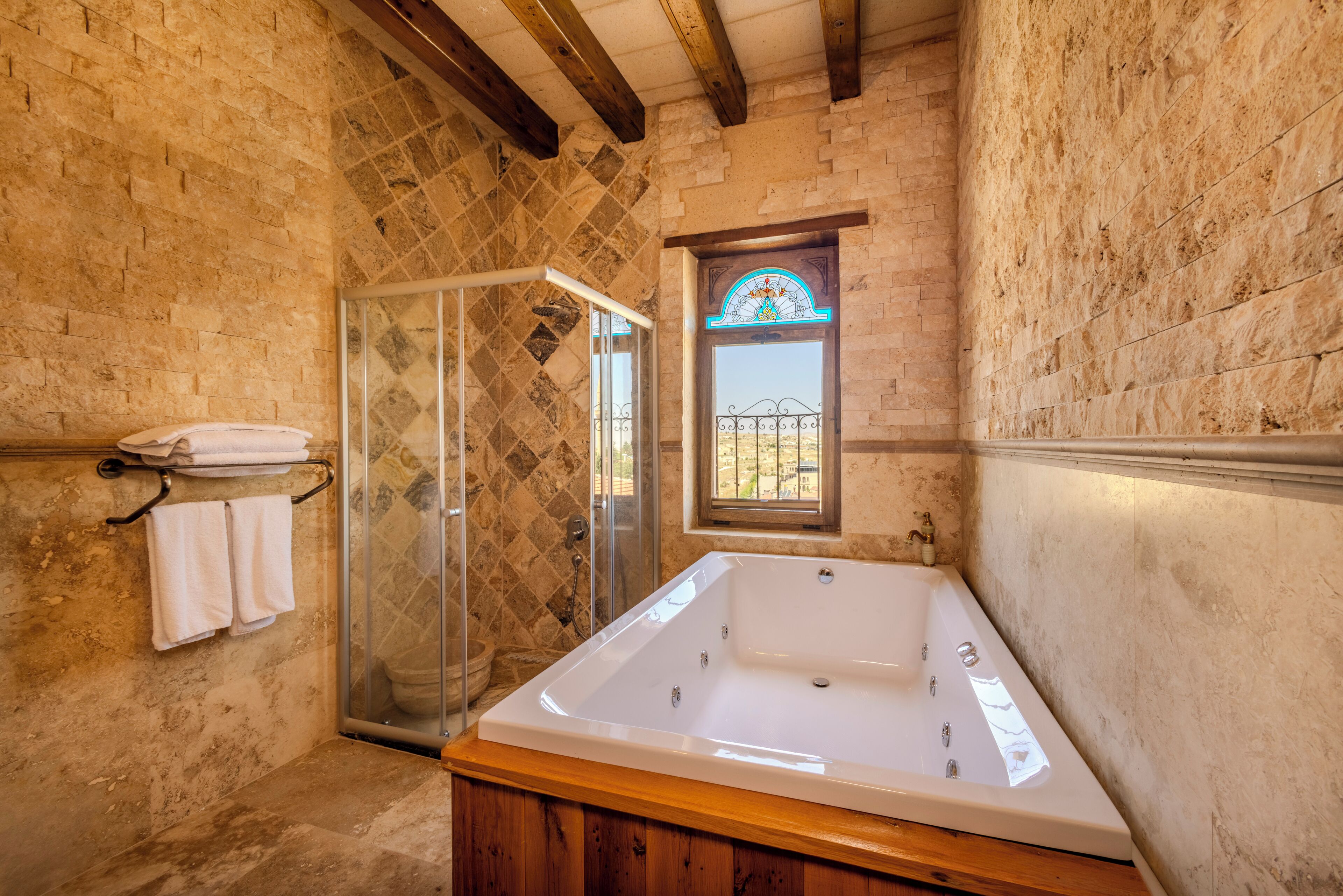 A bathroom with a bathtub, a glass shower enclosure, and a window with a decorative stained glass design.