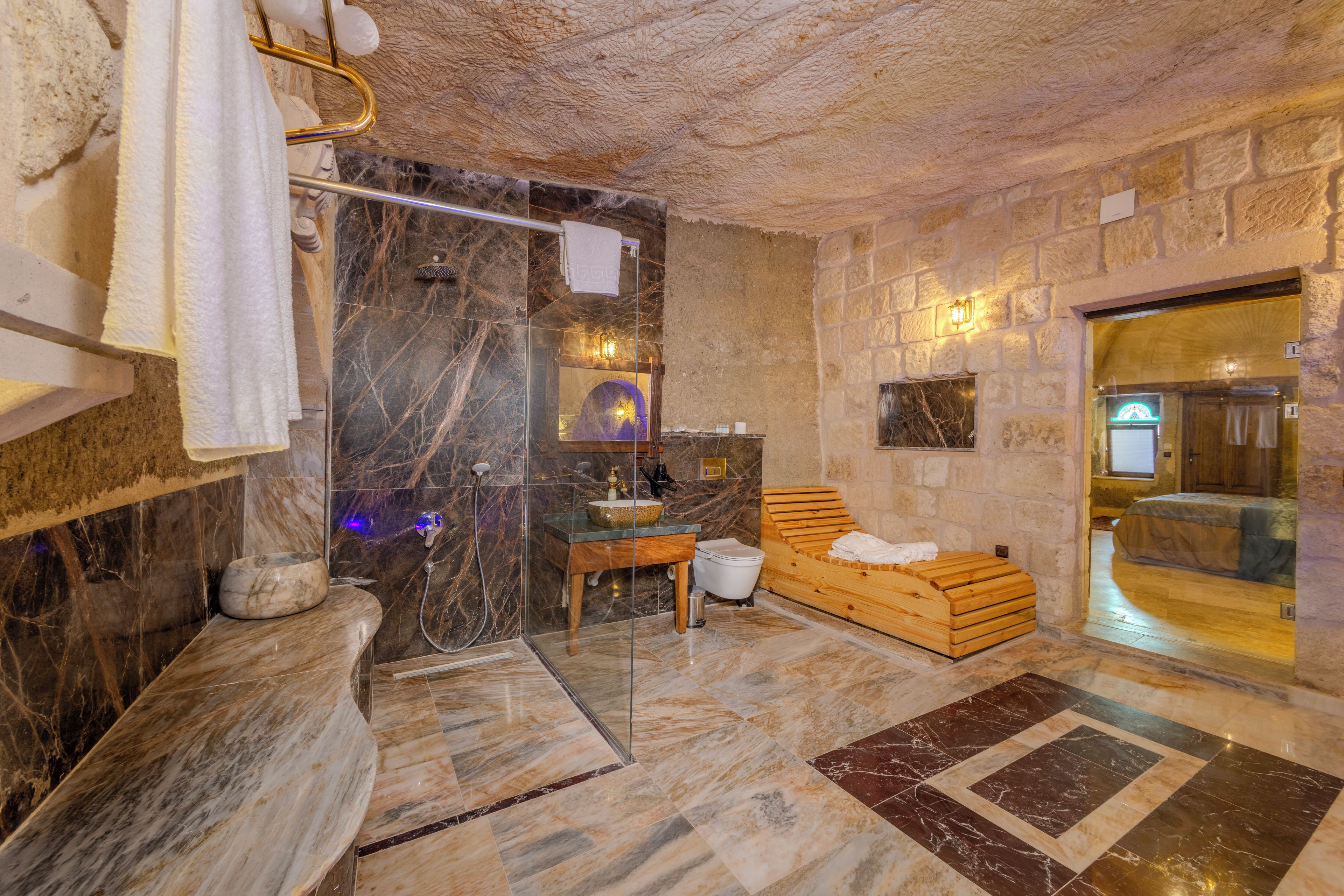 A stone-walled bathroom with a wooden bench, a glass shower enclosure, and a marble floor.
