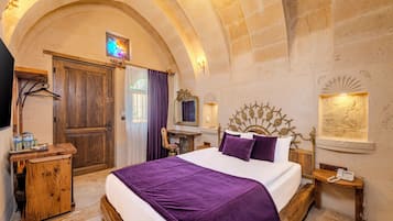 A hotel room with a large bed, a wooden dresser, a vanity with a mirror, and a stone wall.