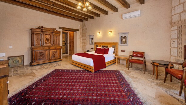 A bedroom with a large bed, a wooden wardrobe, a red patterned rug, and a stone wall. - Karis Cave Cappadocia (Ürgüp)