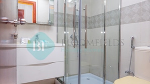 Een moderne badkamer met een glazen douchecabine, een toilet en een wastafel met lades.