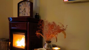 A cozy room with a wood-burning stove, a clock, a vase with dried flowers, and a table with two mugs and a bowl of snacks. - Double bedroom Leonida in B&B (Gaeta)