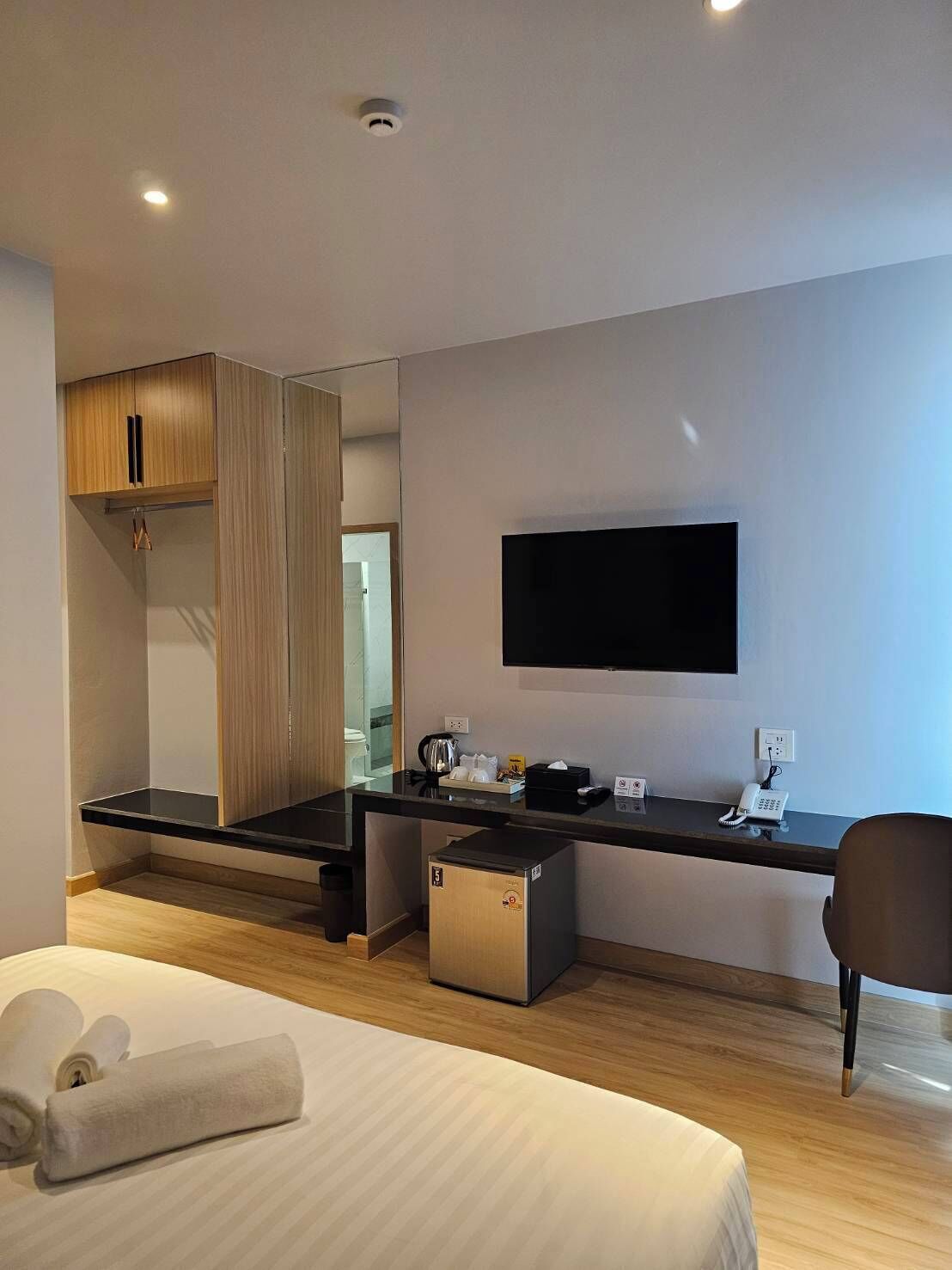 Una habitación de hotel moderna con una cama, un escritorio con televisor de pantalla plana, un mini bar y una kitchenette pequeña.