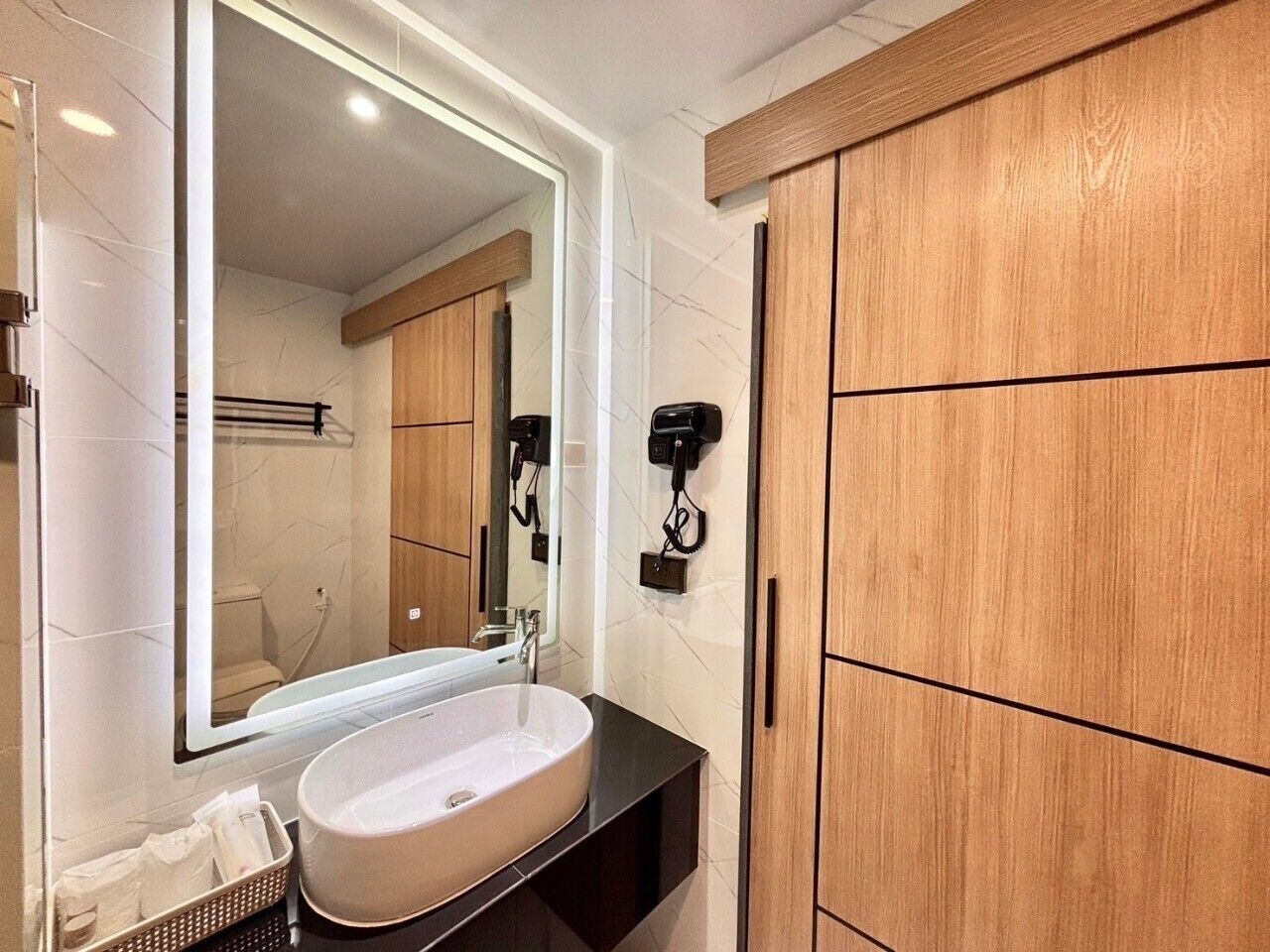 Un baño moderno con un espejo grande, un lavamanos blanco y armarios de madera.