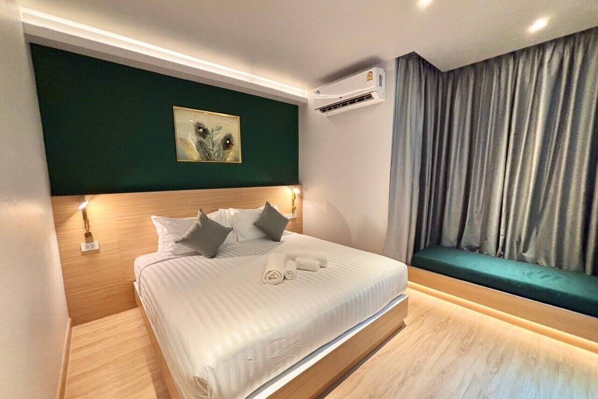 A modern hotel room with a large bed, a bedside table, an air conditioning unit, and a view of the city through curtains.