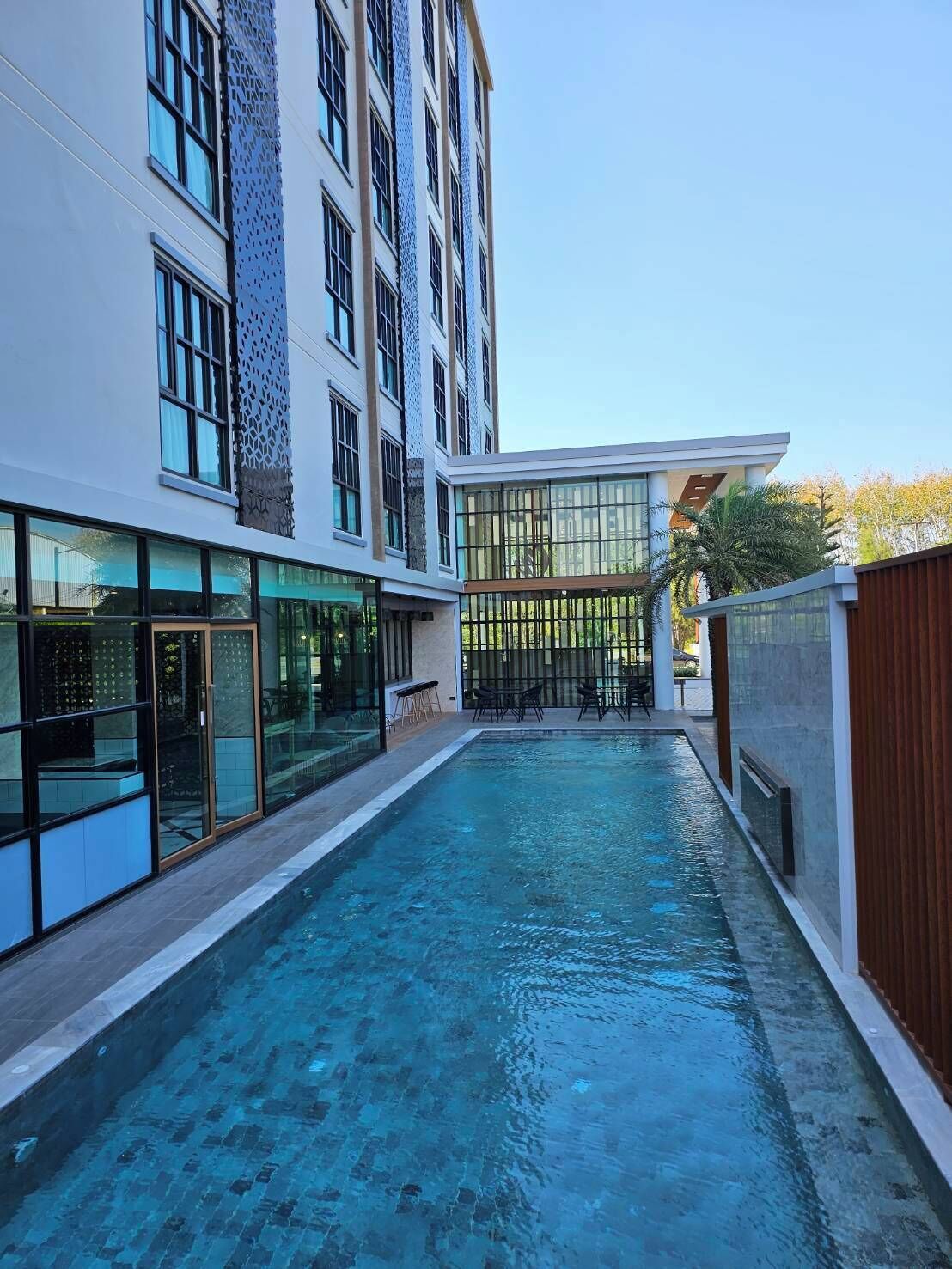 A modern building with a swimming pool, large windows, and a covered area with outdoor seating.
