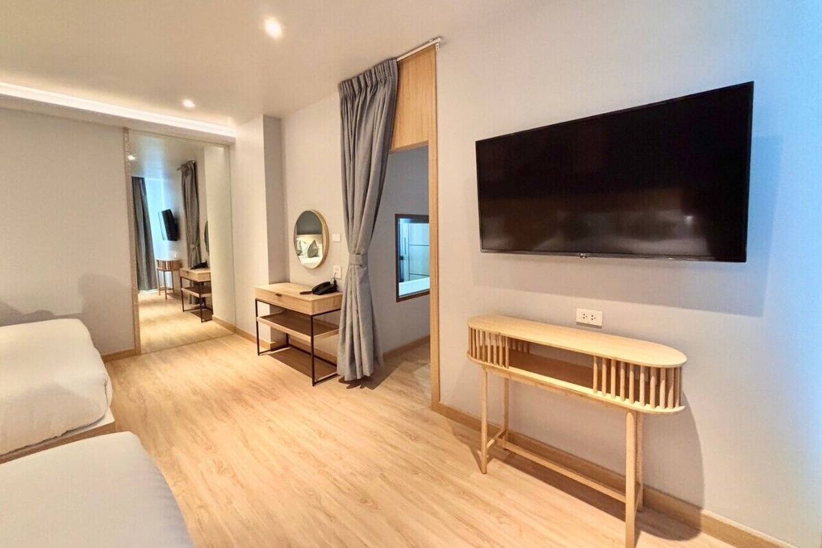A modern hotel room with a large bed, a desk with a computer, a TV mounted on the wall, and a small table.