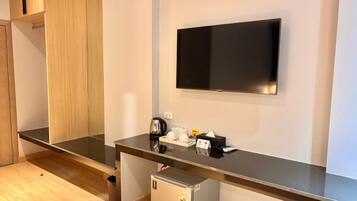 Quarto de hotel moderno com televisão de tela plana na parede, minibar, cafeteira e lixeira.