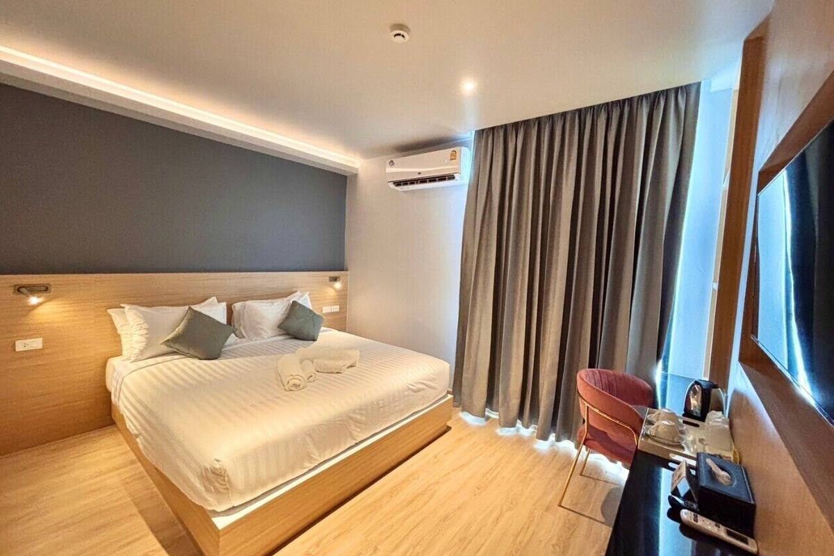 A modern hotel room with a large bed, a desk with a chair, and a window with curtains.