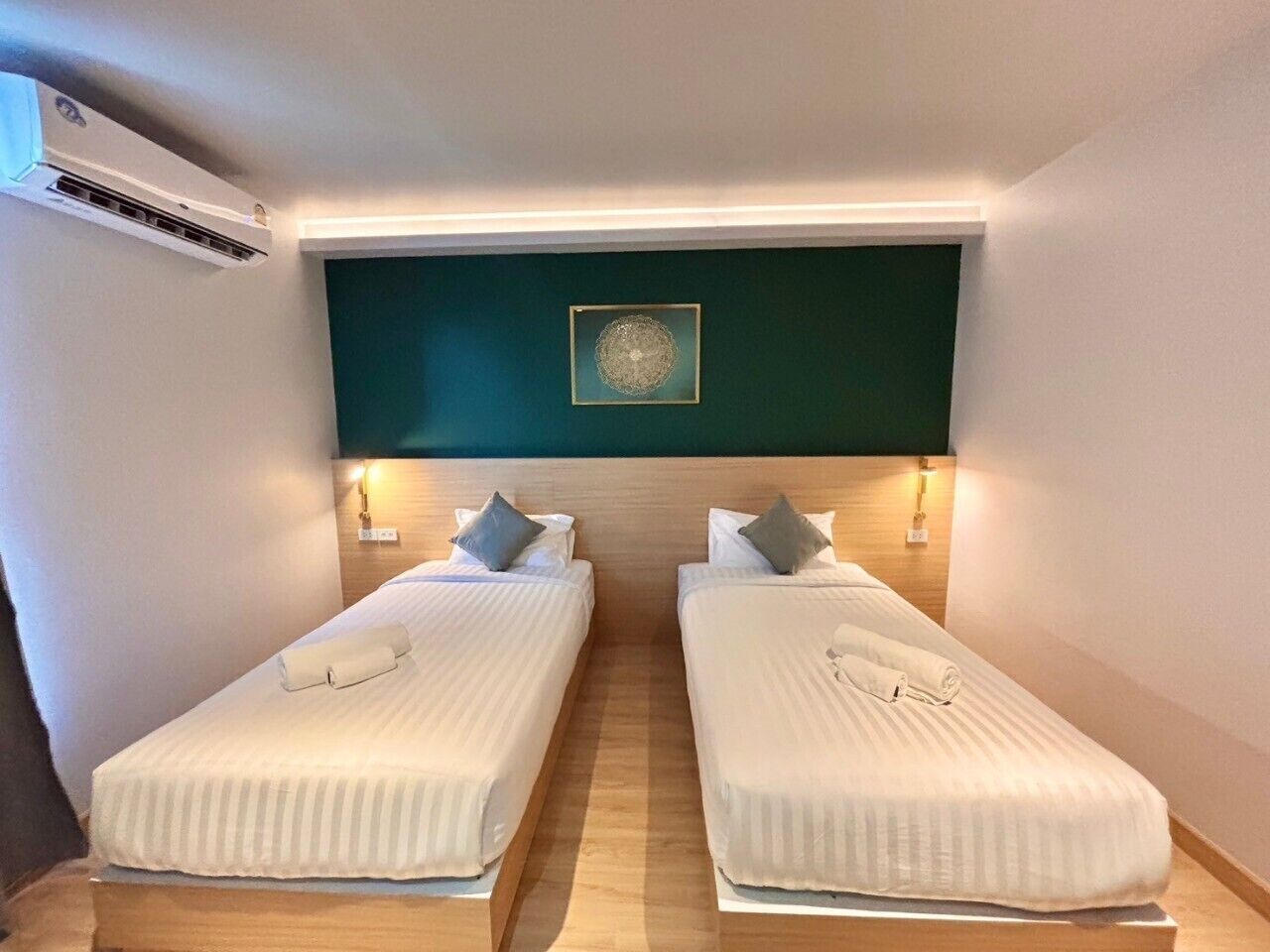 Habitación de hotel con dos camas individuales, una pared de acento verde oscuro y una obra enmarcada sobre las camas.