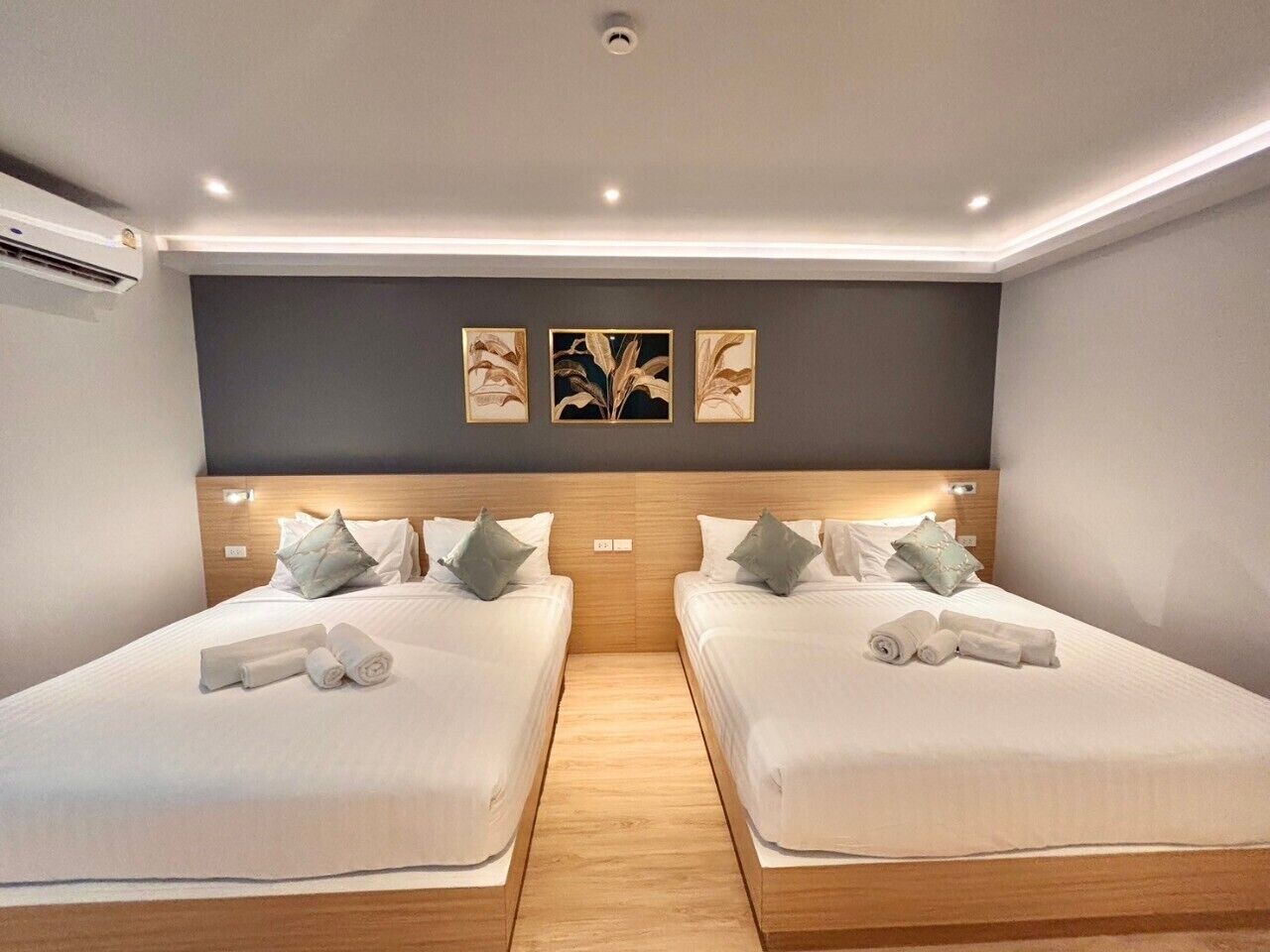 A hotel room with two beds, each with pillows and towels. There are wall-mounted light fixtures and a ceiling light.