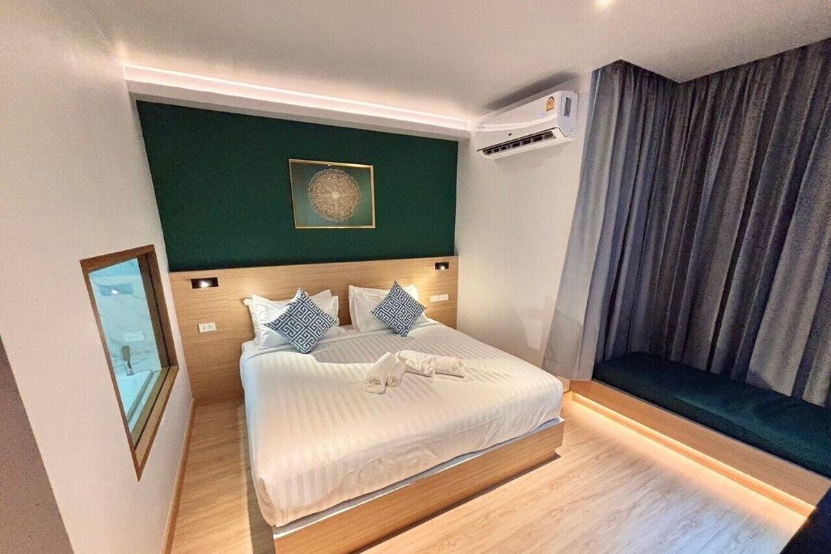 A hotel room with a bed, a bedside table, a wall-mounted air conditioner, a window with a view, and a curtain.