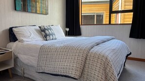 A neatly made bed with a white and patterned blanket, a pillow with a giraffe design, and a wall-mounted abstract painting.