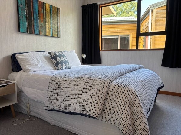 A neatly made bed with a white and patterned blanket, a pillow with a giraffe design, and a wall-mounted abstract painting.