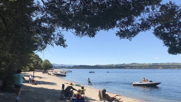 A beach with people relaxing, boats on the water, and a clear sky.