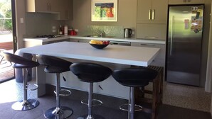 A modern kitchen with a central island, bar stools, stainless steel appliances, and a hanging light fixture.