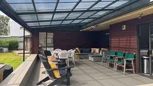 A covered outdoor patio with a glass roof, wooden deck, and outdoor furniture.