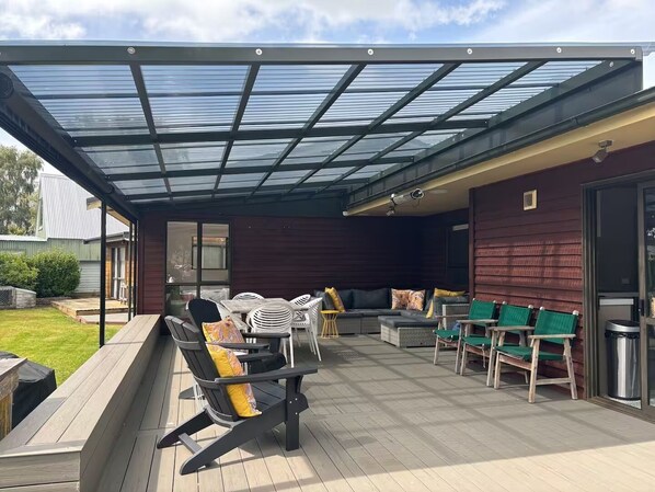 A covered outdoor patio with a glass roof, wooden deck, and outdoor furniture.