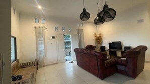 A living room with a red sofa, a wooden bench, a TV, and a sound system. - Hotel O Bogor near Taman Safari formerly Villa Ruko (Cisarua)