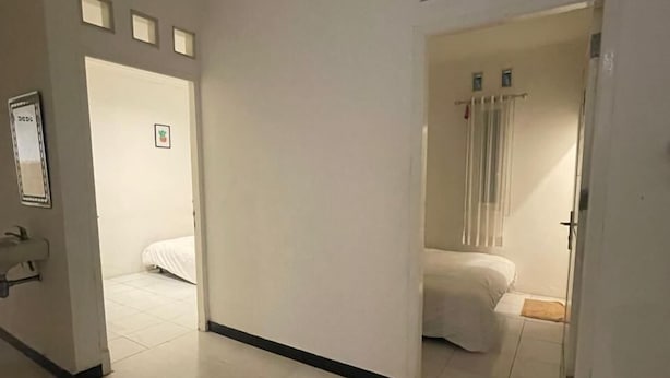A hotel corridor with a bed in the adjacent room, a mirror, and a door leading to another room. - Hotel O Bogor near Taman Safari formerly Villa Ruko (Cisarua)
