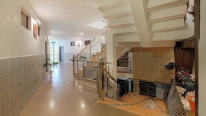 Un hallo espacioso con piso pulido, una escalera con barandas de cristal y un panel decorativo en la pared.