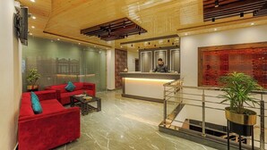 Un vestíbulo moderno con mostrador de recepción, sofás rojos, suelo de mármol y techo de madera.