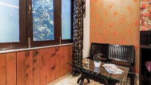 Una habitación con una pared de paneles de madera, una mesa de vidrio con una revista, dos bancos negros y una ventana con cortinas.