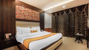 Habitación de hotel con una cama grande, una mesita de noche, una mesa y una cortina con estampado floral.
