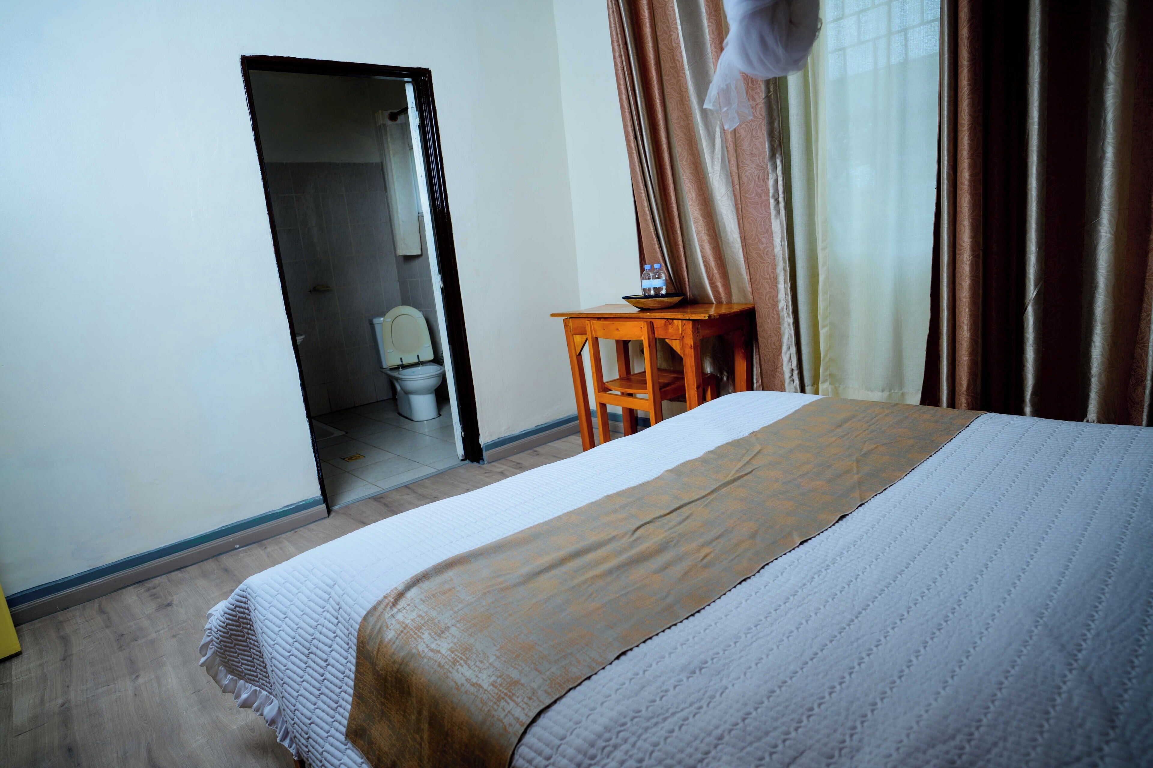 A hotel room with a bed, a wooden nightstand, a mirror, and a view of the bathroom.