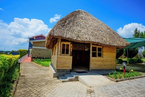 A wooden house with a thatched roof, a paved pathway, and a garden with yellow flowers.
