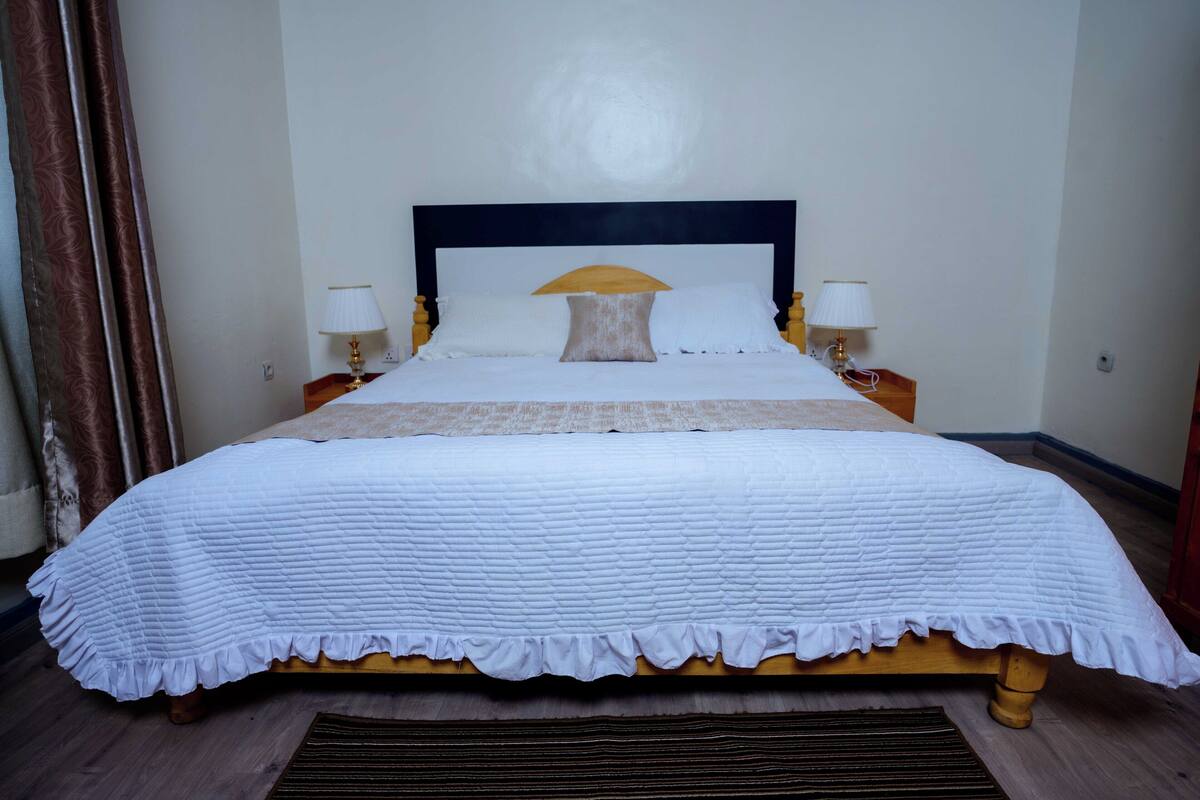 A neatly made bed with a white quilt, two bedside lamps, and a wooden headboard.