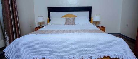 A neatly made bed with a white quilt, two bedside lamps, and a wooden headboard.