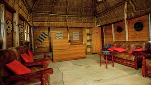 A traditional wooden interior with a thatched roof, leather sofas with red cushions, and woven mats on the floor. - Quality Inn Motel (Busasamana)