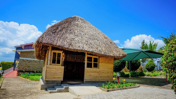 A wooden house with a thatched roof, a paved entrance, and a green umbrella nearby. - Quality Inn Motel (Busasamana)