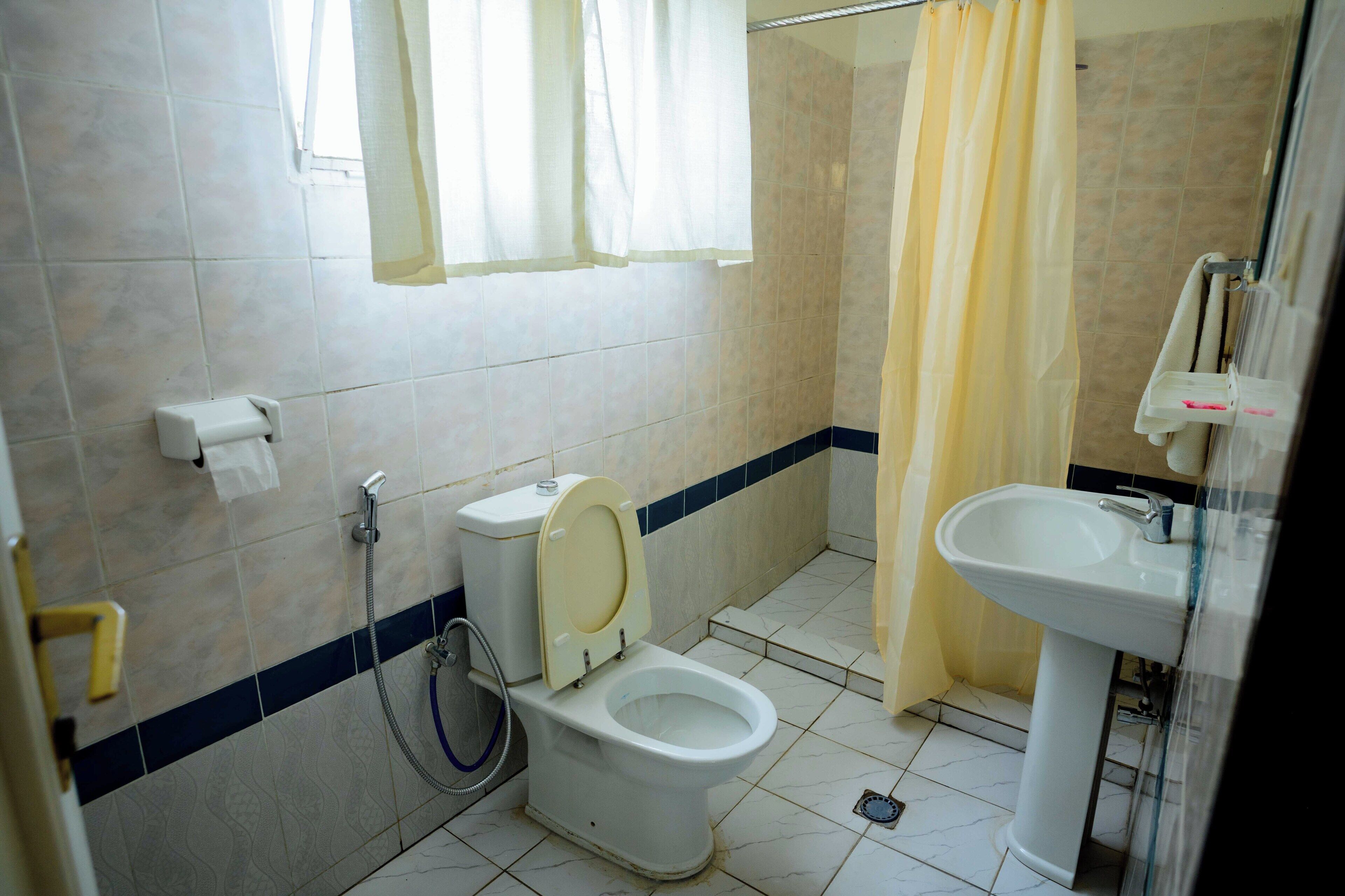 A bathroom with a toilet, shower curtain, sink, and a window with curtains.