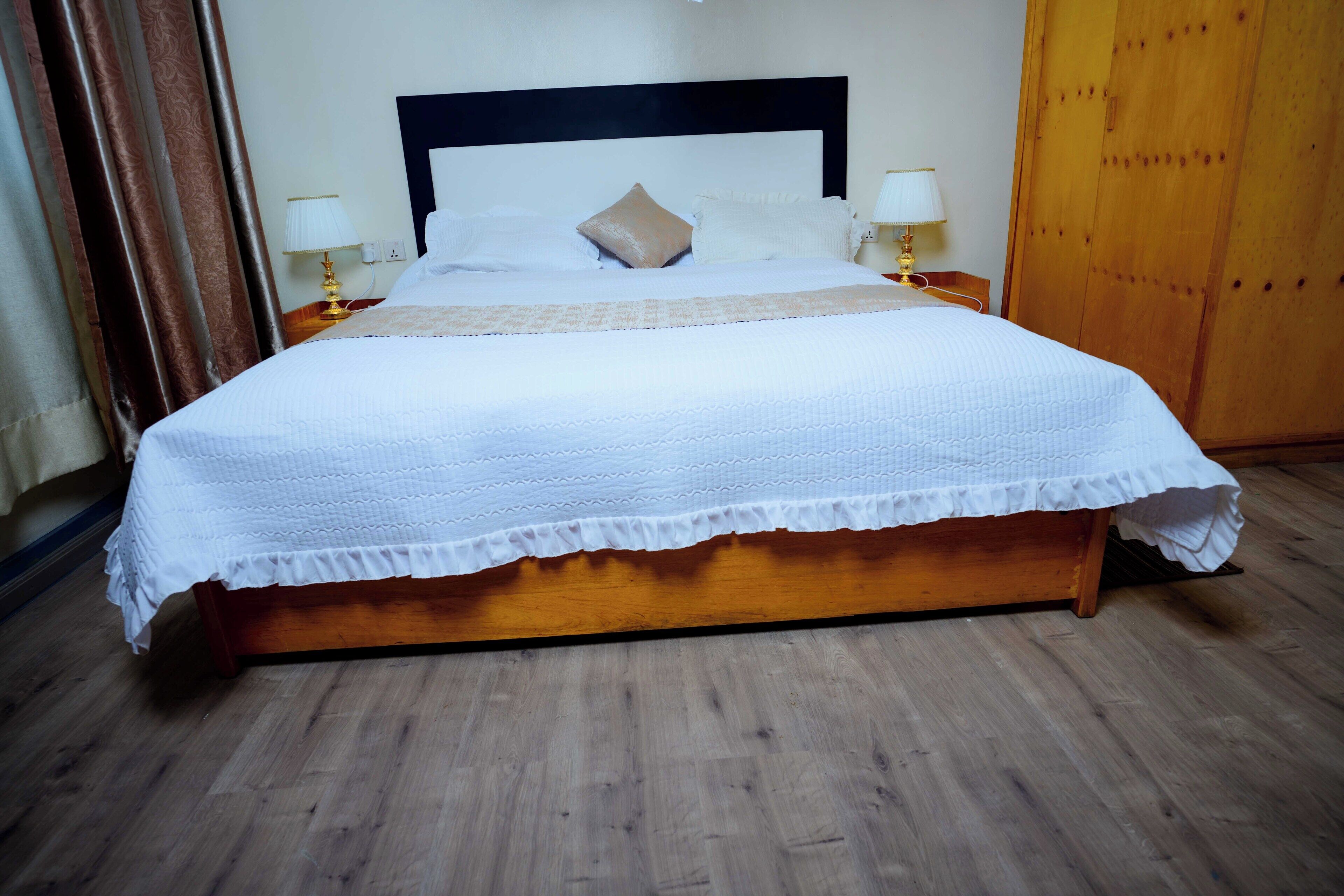 A neatly made bed with a white bedspread and pillows, a wooden headboard, and two bedside lamps.