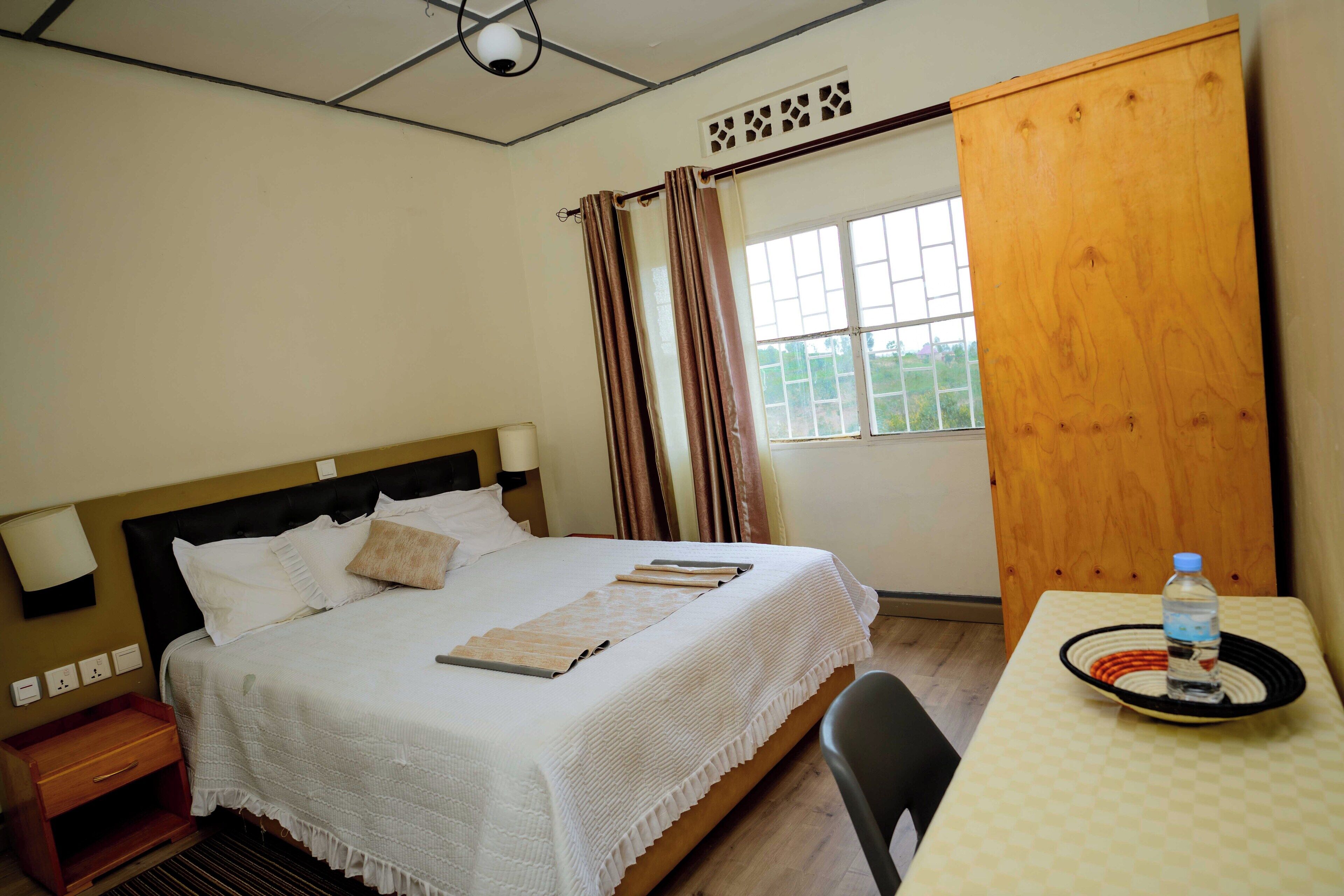 A neatly made bed with a white bedspread, a bedside table with a lamp, and a window with curtains.
