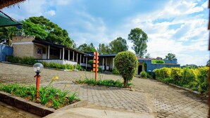 A courtyard with a brick pathway, a small tree, and a building with a porch. - Quality Inn Motel (Busasamana)
