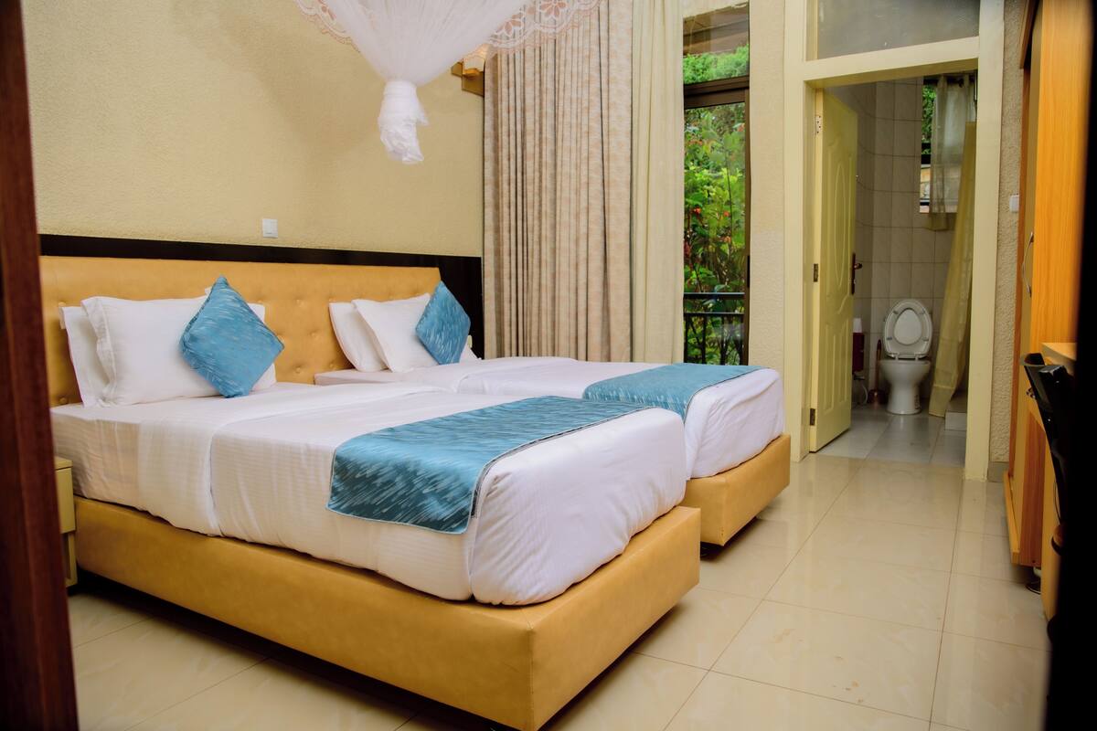 A hotel room with two beds, a wooden headboard, a canopy, and a view of the outdoors.