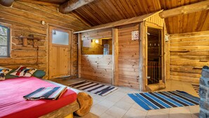 Ein Blockhausszimmer mit einem Bett, einer Holztür, einem Fenster und einem kleinen Tisch.