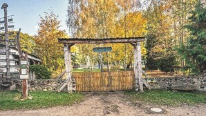 Ein rustikales Holztor mit einem Schild, umgeben von Bäumen und einer Steinmauer.