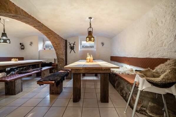A rustic dining area with a wooden table, benches, and a stone wall.