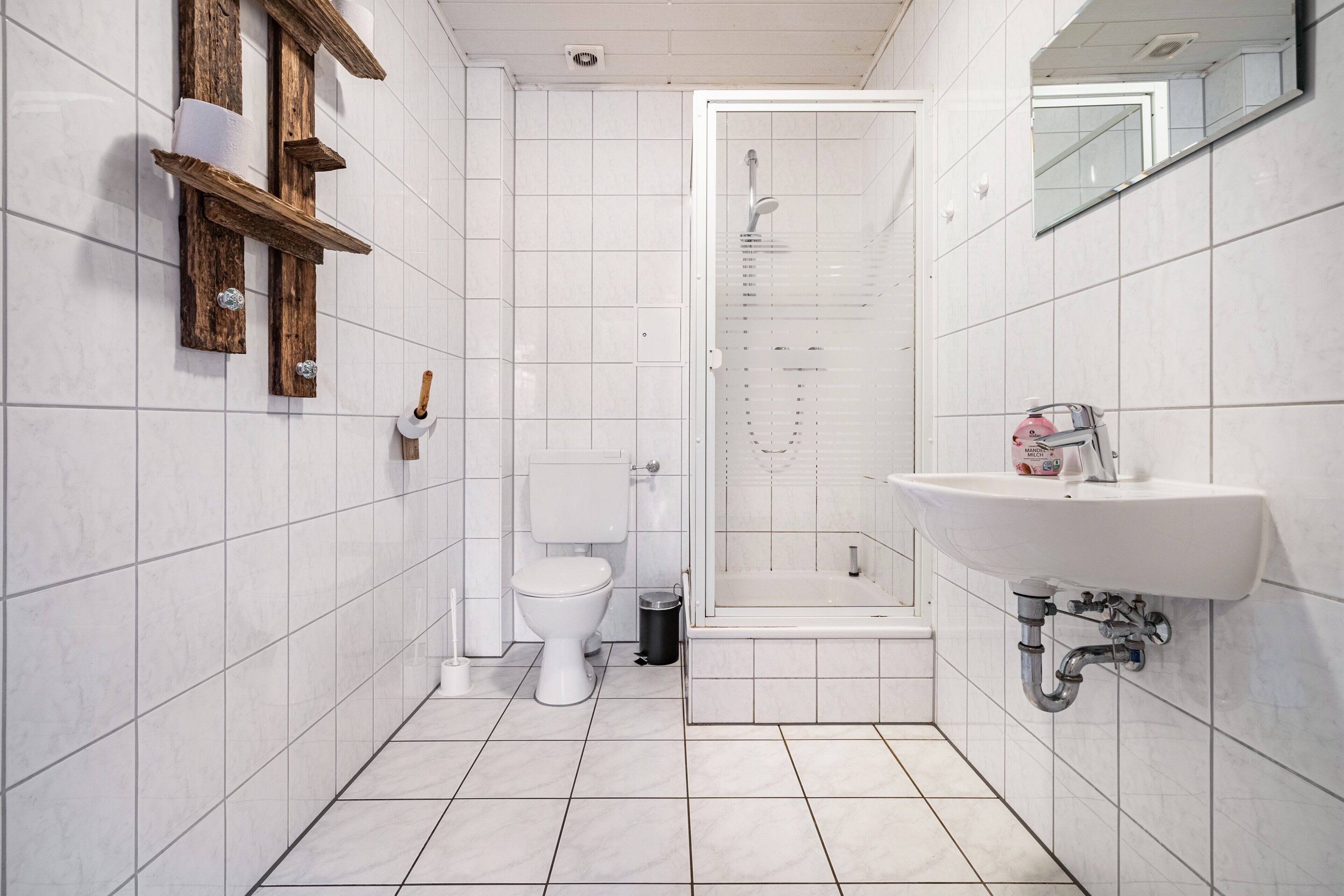 A bathroom with white tiled walls, a toilet, a shower, and a sink.