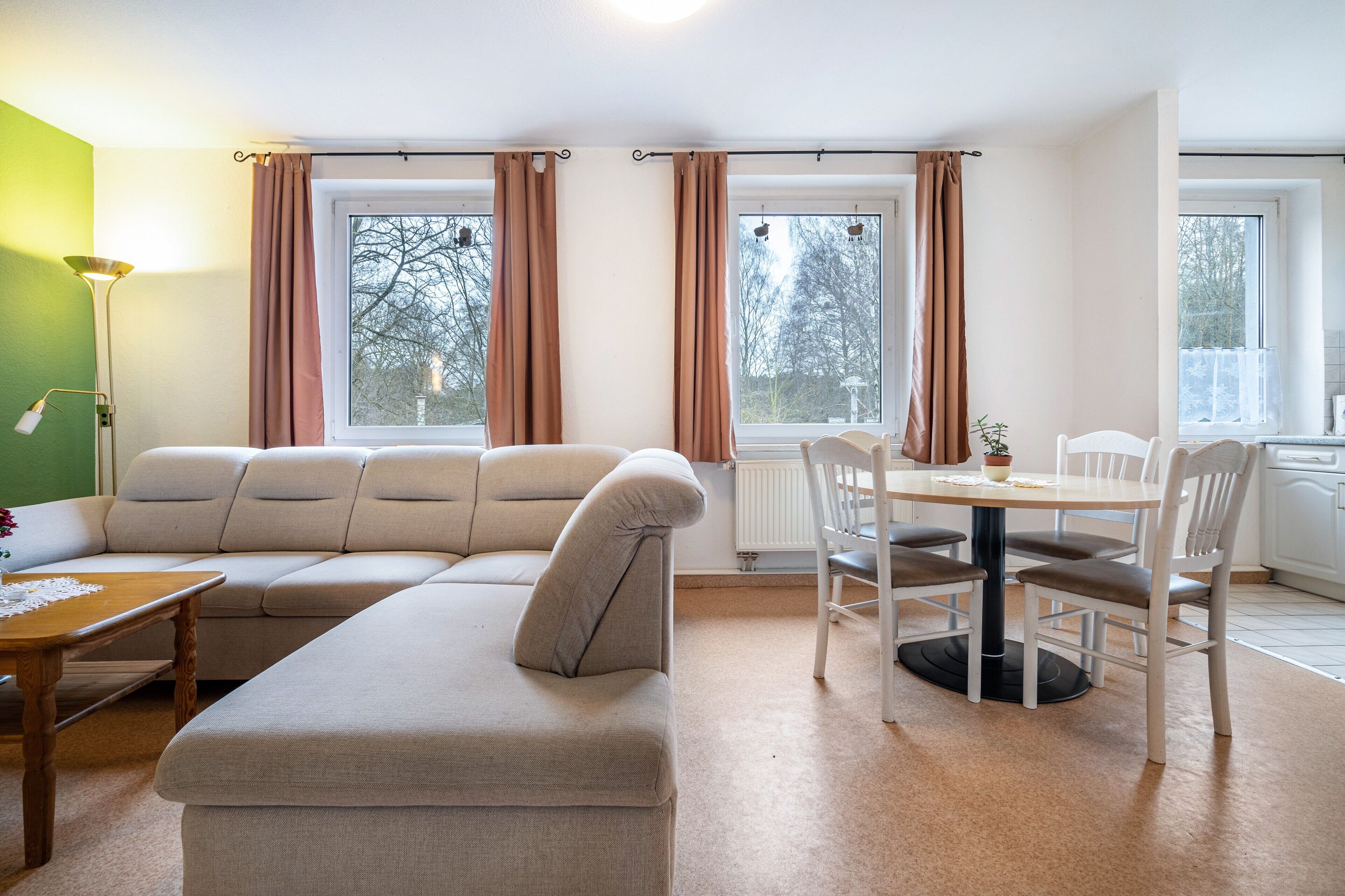 A modern living room with a sectional sofa, a dining table with chairs, and large windows with curtains.