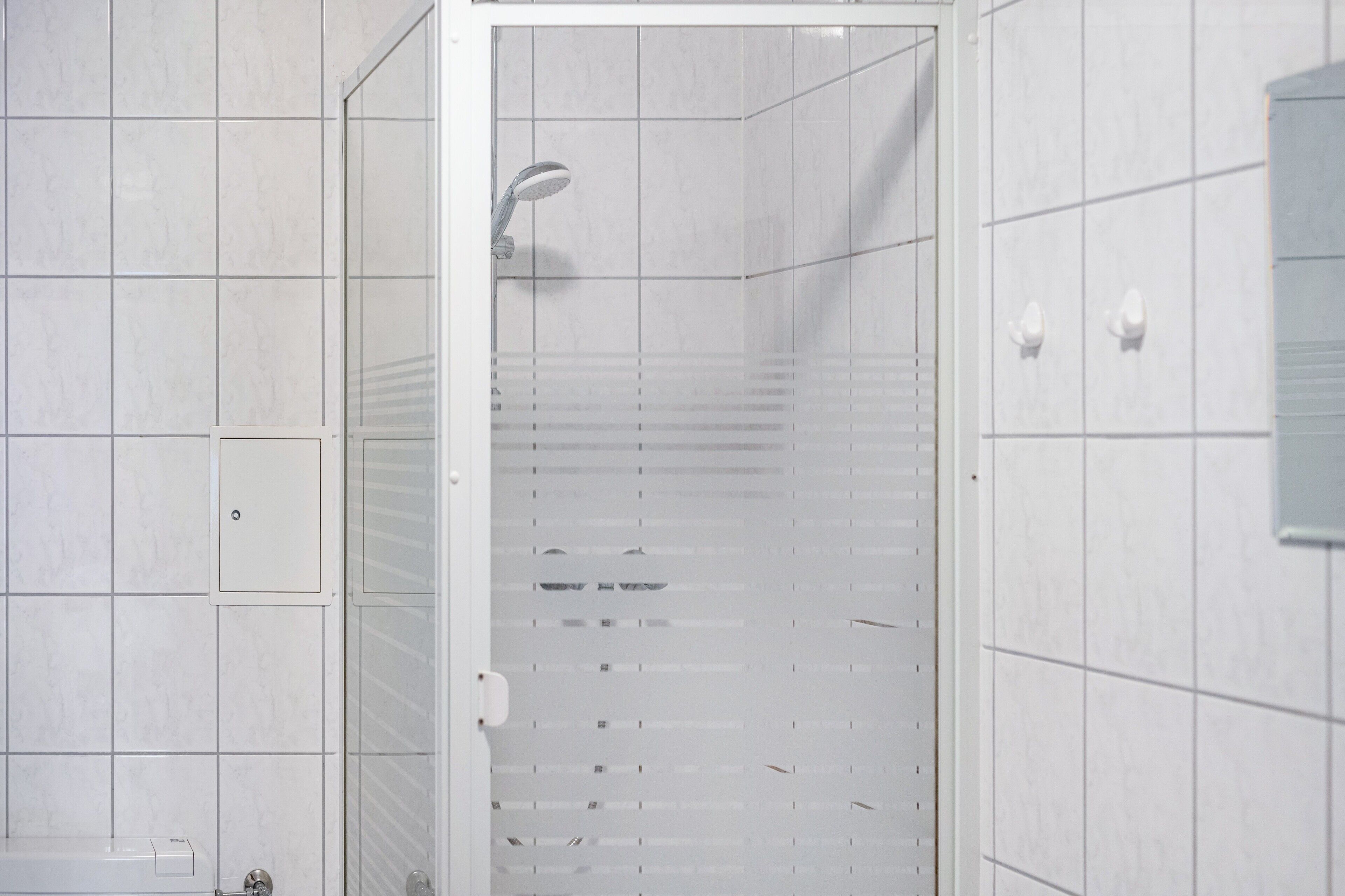 Une douche avec une porte en verre, des murs recouverts de carreaux blancs et un panneau de commande visible.