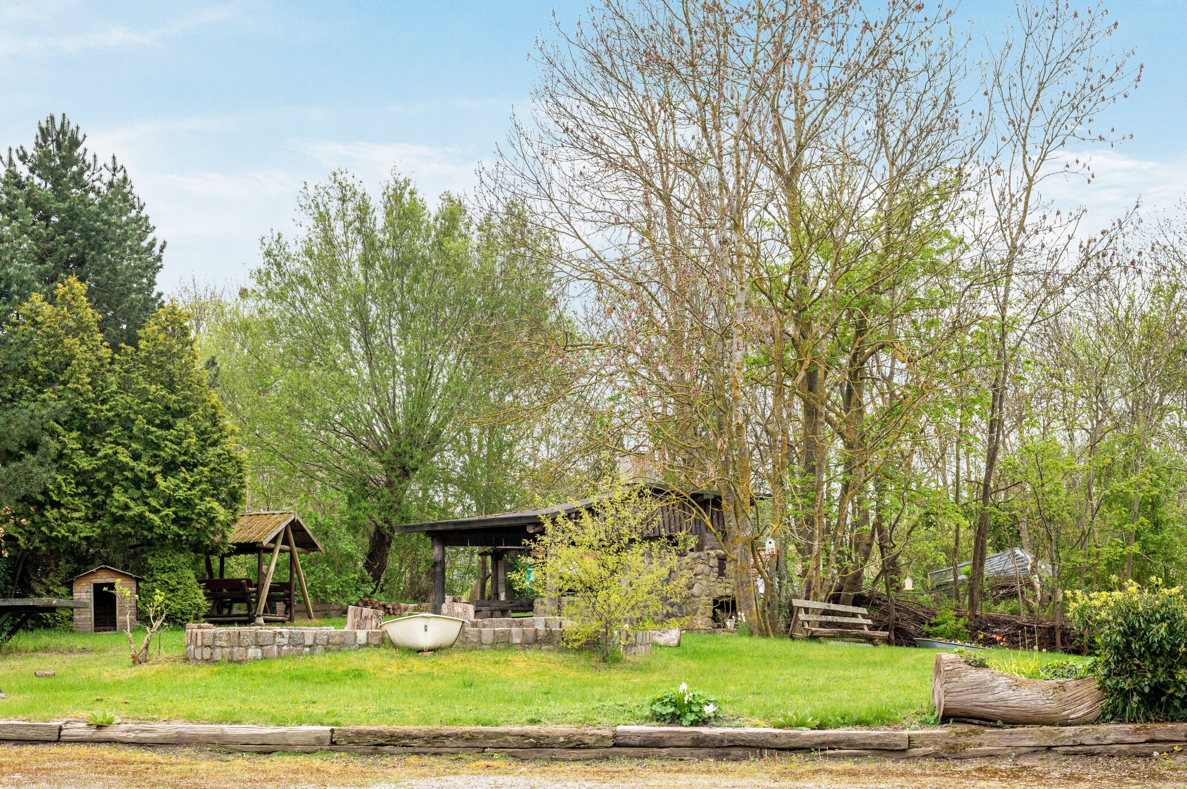 A rustic cabin with a wooden deck, surrounded by trees and a small pond.