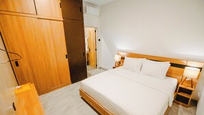 A hotel room with a large bed, wooden headboard, bedside tables with lamps, and a wardrobe. - Queenara Local House (Carangsari)
