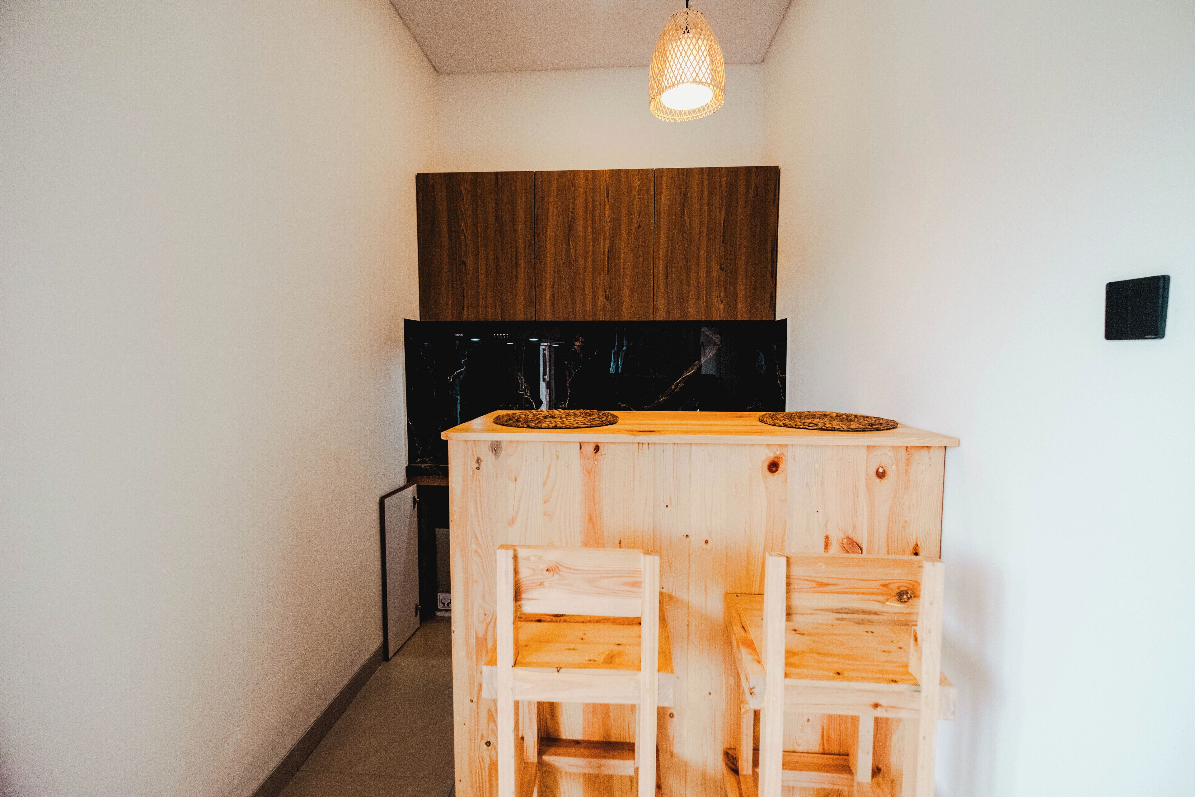 Eine kompakte Küche mit einer Holzausziehtheke und zwei Barhocker, einem schwarzen Kühlschrank und einer Pendelleuchte.