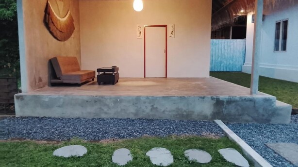 Un espacio de estar al aire libre techado, con una plataforma de concreto, un banco y una mesa pequeña.