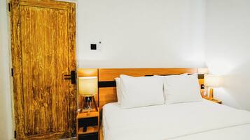 Habitación de hotel con puerta de madera, cama con ropa blanca, dos lámparas de noche y una mesita de noche.